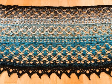 Ombre crocheted scarf in black, grey and blue with open lace stitch on wooden floor