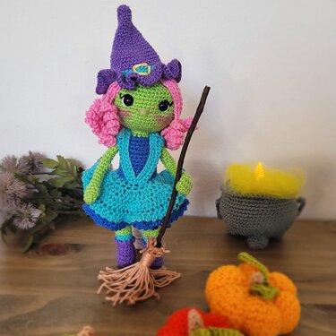 Gehäkelte Hexen‑Amigurumi mit türkisem Kleid, lila Hut, rosa Locken, Besen und gehäkelten Kürbissen