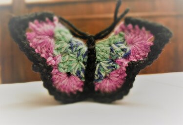 Gehäkelter Schmetterling mit Flügeln in Rosa, Grün, Violett und schwarzem Körper/Rand