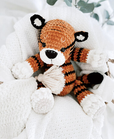 Handgehäkelter orange‑schwarz gestreifter Amigurumi‑Tiger auf weißer, flauschiger Decke