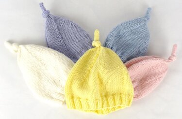 Fünf gestrickte Babymützen in Pastellfarben: gelb, weiß, rosa, hellblau, flieder mit Knoten oben