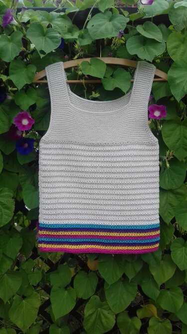 Hellgraues gestricktes ärmelloses Top mit mehrfarbigen Streifen am Saum an einem Holzbügel vor grünen Blättern