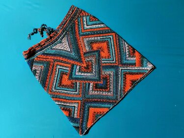 Gestricktes Dreieckstuch mit konzentrischen Quadraten in Orange, Petrol und Blau auf blauem Hintergrund