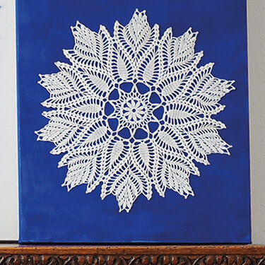 Rundes weißes Häkel-Deckchen mit Blättermuster auf blauem quadratischem Hintergrund