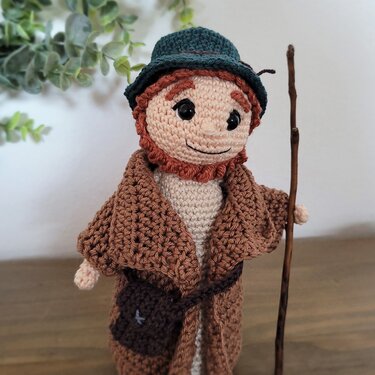 Amigurumi-Krippenfigur: gehäkelter Hirte mit Mantel, Hut, Tasche und Stab.