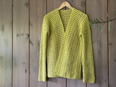 Lime-green open-front crochet cardigan with V-neck and long sleeves hanging on wooden hanger