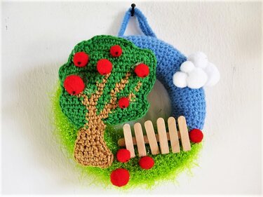 Gehäkelter Türkranz mit Apfelbaum, roten Äpfeln, Mini-Holzzaun und blauen Wolken