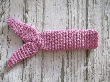 Nahaufnahme eines schnell gehäkelten rosa Bands mit zwei Zipfeln auf hellem Holz