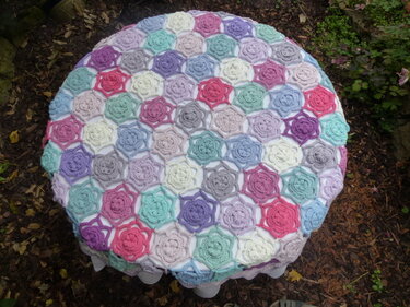 Rundes gehäkeltes Deckchen aus sechseckigen Blumenmotiven in Pastellfarben auf einem Außentisch.