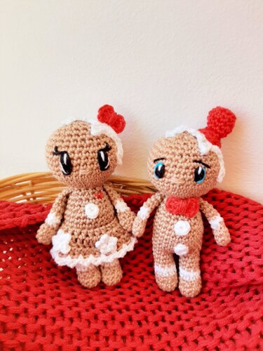 Zwei gehäkelte Lebkuchen-Amigurumi mit weißem Zuckerguss und roten Akzenten auf roter Decke