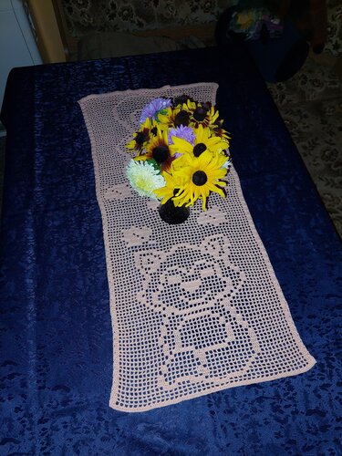 Beiger gehäkelter Tischläufer mit Katzenmotiv auf dunkelblauem Untergrund und Blumenstrauß