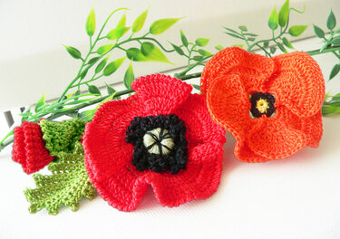 Gehäkelte Mohnblumen in Rot und Orange mit gehäkeltem grünem Blatt und Dekozweigen