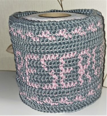 Gehäkelte Hülle in Grau und Rosa um eine Toilettenpapierrolle