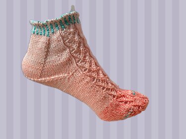 Nahaufnahme einer lachsfarbenen, kurzen Socke mit türkisen Details und einem Lochmuster auf dem Fußrücken.