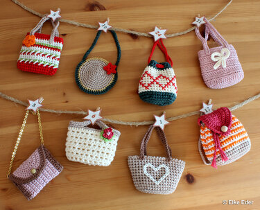 Eight small crocheted bags hanging on twine with numbered star tags, forming an advent calendar display on a wooden surface.