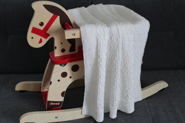 Weiße gestrickte Babydecke drapiert über einem hölzernen Schaukelpferd