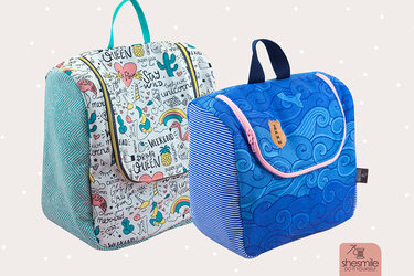 Zwei genähte Stofftaschen mit Reißverschluss: eine mit Einhorn- und Regenbogenmotiven, eine mit blauem Wellendesign und Leuchtturm