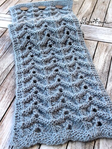 Light blue knitted collar scarf with a wavy eyelet pattern and three wooden buttons, laid on a wooden surface.