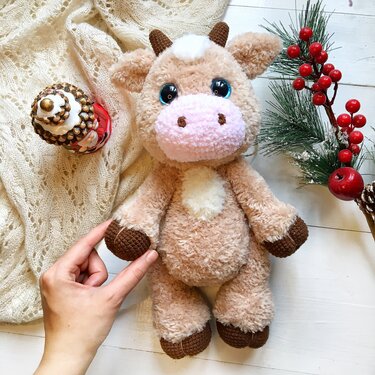 Close view of crocheted cow amigurumi showing yarn texture and a hand for scale