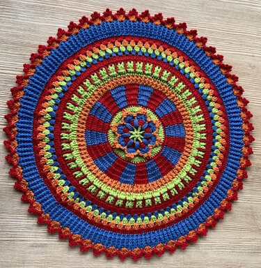 Detailaufnahme eines runden Häkelmusters mit abwechselnden Runden in Blau, Rot, Orange und Grün