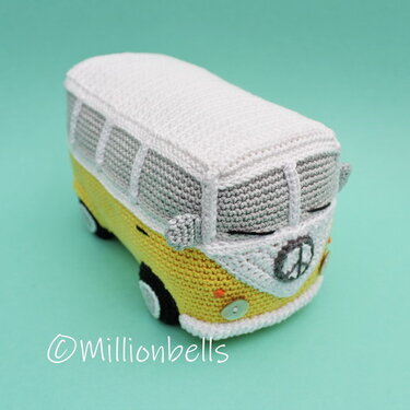 Yellow-and-white hand-crocheted amigurumi camper van with stitched windows and a peace sign on the front