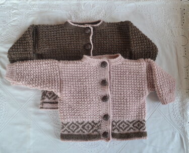 Gestrickte Babyjacken in Rosa und Braun auf weißer Decke