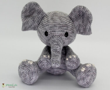 Sitzender grauer gehäkelter Amigurumi-Elefant mit großen Ohren und schwarzen Augen auf hellem Hintergrund.