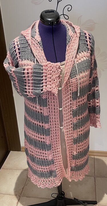 Gehäkelter Longcardigan in Rosa und Grau mit Kapuze, offenem Streifenmuster und dekorativen Verschlüssen.