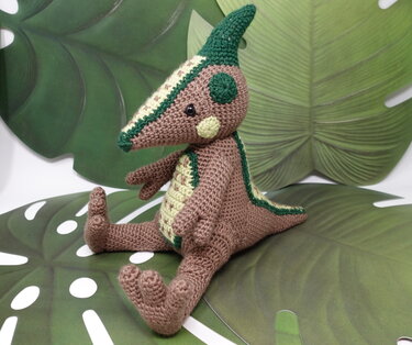 Sitzendes gehäkeltes Dino-Amigurumi in Braun mit grünem Kamm und hellem Bauchmuster