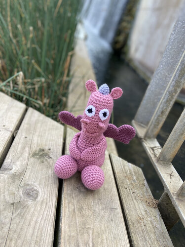 Sitzender Amigurumi-Drache in Rosa zeigt Beine, Flügel und Augen