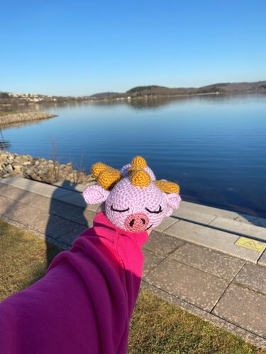 Nahaufnahme eines lila gehäkelten Amigurumi-Dino-Kopfes mit gelben Hörnern, gehalten von einer Hand.