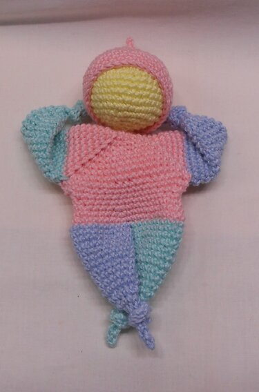 Handgehäkelte Amigurumi-Puppe in Pastellfarben mit geknoteten Enden auf hellem Hintergrund.