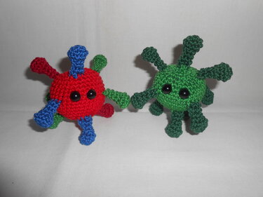 Zwei schnell gehäkelte Amigurumi-Kugeln mit mehreren kurzen Armen, eine rot-blau und eine grün
