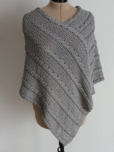 Gehäkelter grauer Poncho mit diagonalen Loch- und Zopfmustern auf einer Schneiderpuppe