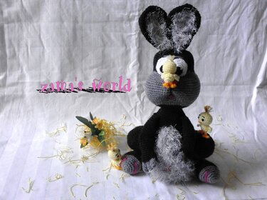 Gehäkeltes Amigurumi-Häschen in Schwarz-Grau mit zwei kleinen gelben Küken vor hellem Stoffhintergrund