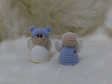 Zwei kleine gehäkelte Engel, einer frontal mit blauem Mützchen und weißem Körper, daneben die Rückansicht eines blauen Engels mit Flügeln und Herzdetail