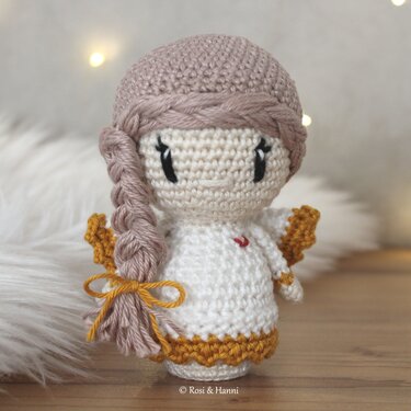 Gehäkeltes Engelchen-Amigurumi in Cremeweiß mit goldenen Flügeln und geflochtenem Zopf