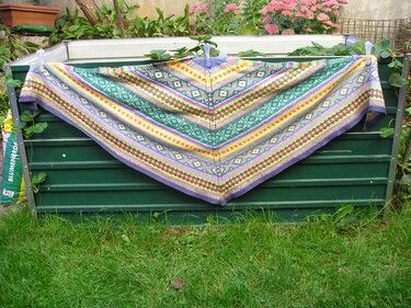 Farbenfrohes gestricktes Dreieckstuch mit Rauten- und Streifenmustern vor grünen Pflanzen