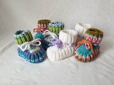 Mehrere Paare handgestrickter Babyschuhe in bunten Farben auf weißem Tuch