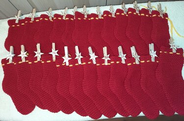 24 rote gehäkelte Säckchen als Adventskalender mit nummerierten Holzstern-Klammern und gelbem Zierband.