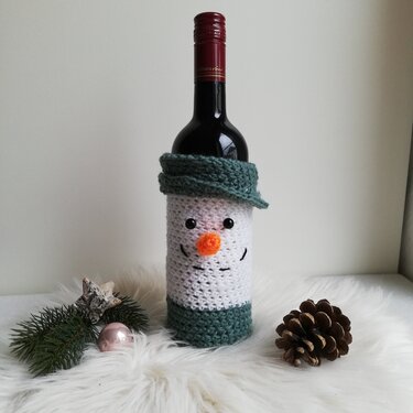 Weinflasche mit gehäkelter Schneemann-Hülle, grünem Schal und Saum, Dekoration mit Tannenzweig und Zapfen
