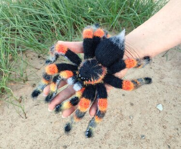 Hand holding a palm-sized crocheted spider amigurumi in black, orange and gray fuzzy yarn