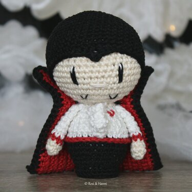 Gehäkelter Vampir‑Amigurumi mit schwarzem Umhang und rotem Futter