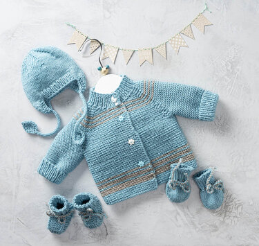Hellblaue gestrickte Babymütze mit Ohrenklappen und Bindebändern, daneben eine Babystrickjacke und Babyschuhe