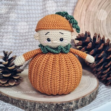 Gehäkeltes Kürbis-Amigurumi mit beigem Kopf, orangefarbenem Körper, grünem Kragen und Mütze.