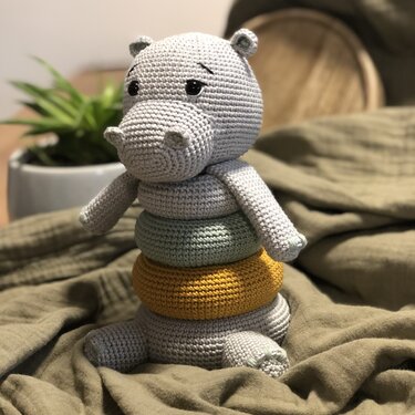 Grau gehäkeltes Nilpferd mit gestapelten mint- und senfgelben Ringen auf Stoff