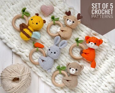 Five crochet animal teething rings (bee, deer, fox, bunny, bear) attached to wooden rings on a cream textured blanket