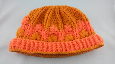 Orange- und lachsfarbene gehäkelte Mütze mit Noppen- und Rippenmuster auf hellem Hintergrund.
