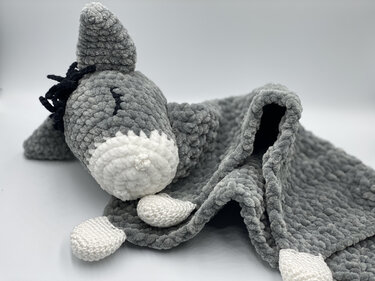 Grey crocheted donkey baby snuggle blanket with white snout and black mane on a white background.