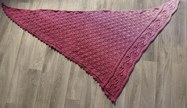 Pink ombre crocheted triangle shawl with basketweave texture and scalloped edge on a wooden floor